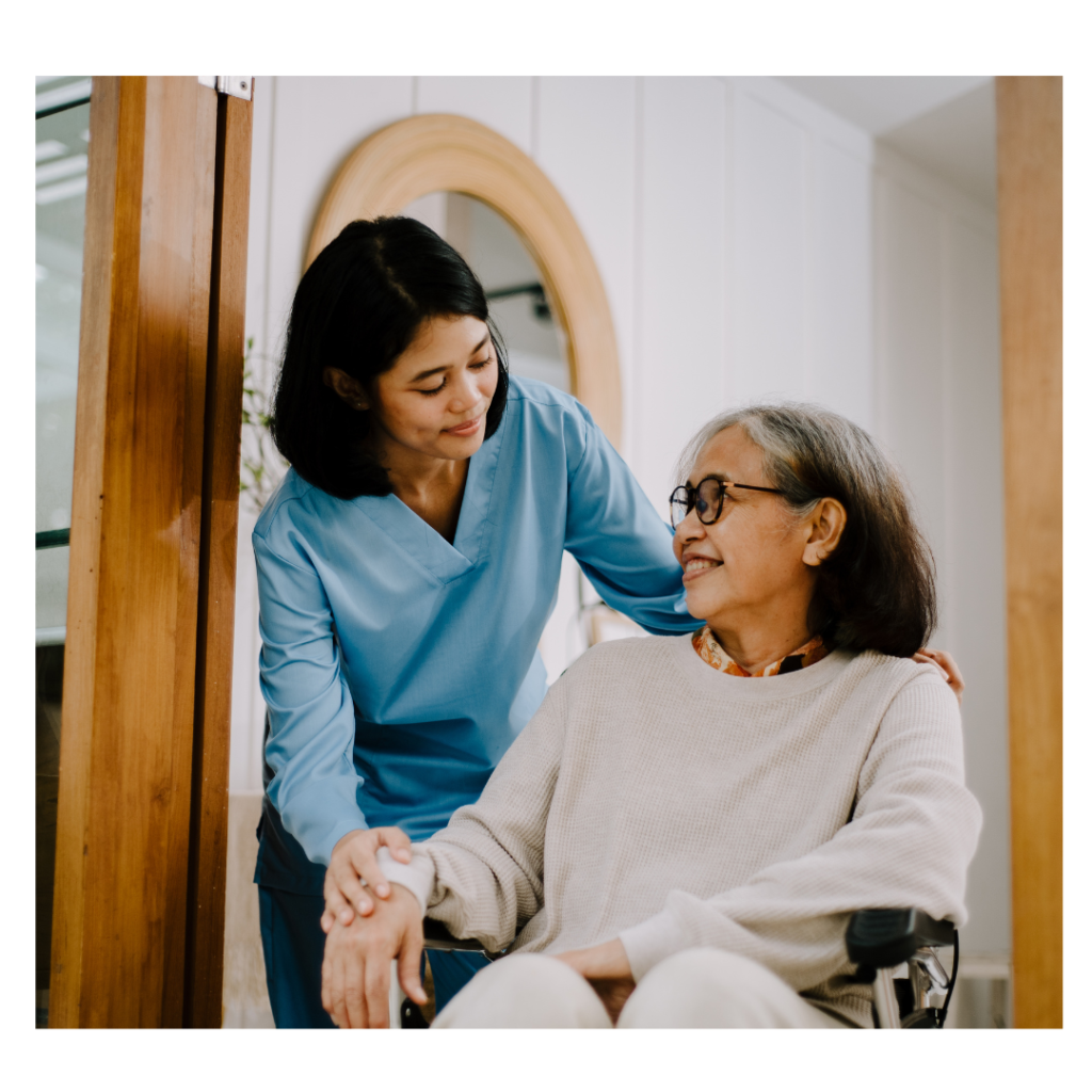 A caregiver warmly interacts with an elderly woman in a wheelchair.
