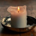 A lit white candle melting in a shallow dish.