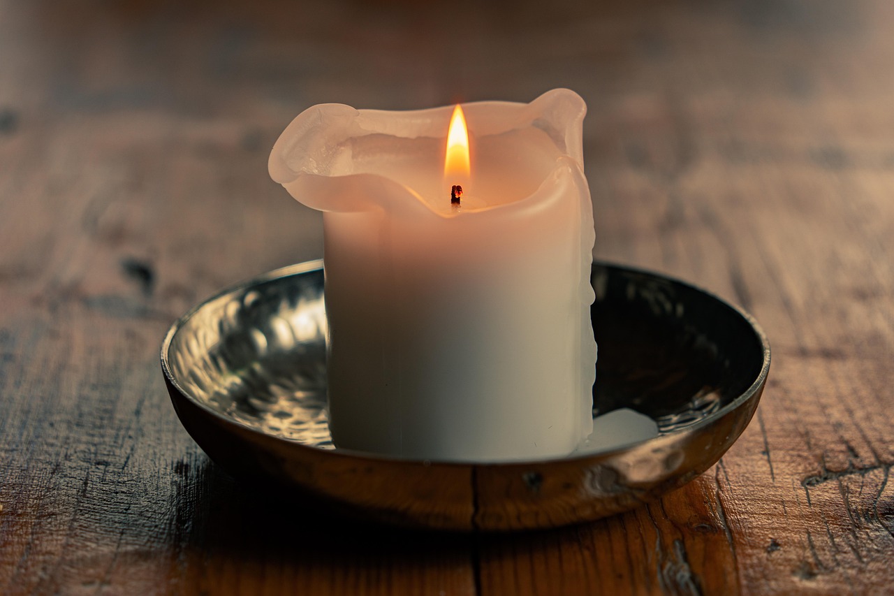 A lit white candle melting in a shallow dish.